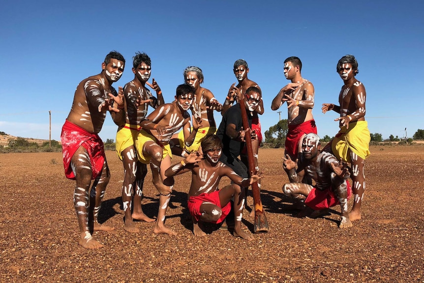 A group of 10 Indigenous men and boys pose painted up for a dance.