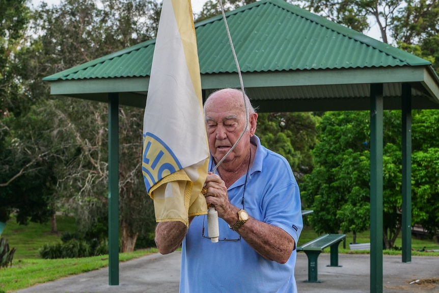 Elderly man hangs a flag up a flagpole.