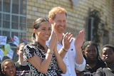 Prince Harry and his wife Meghan are clapping and smiling