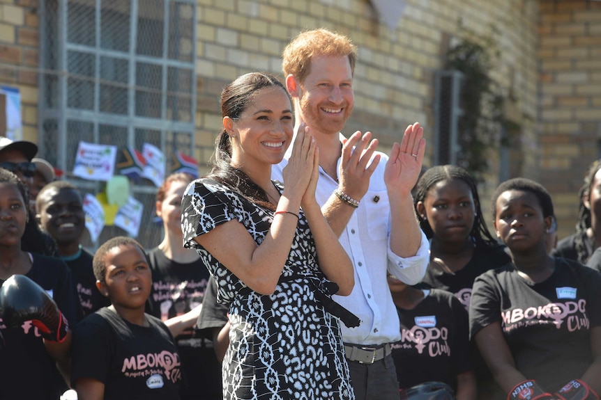 Prince Harry and his wife Meghan are clapping and smiling