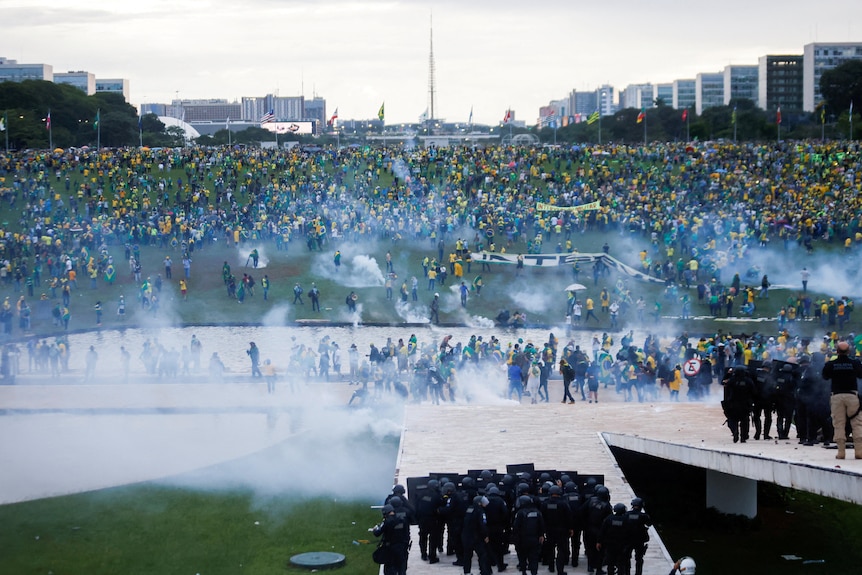 A crowd of people wearing yellow shirts mill around a lawn covered in smoke.