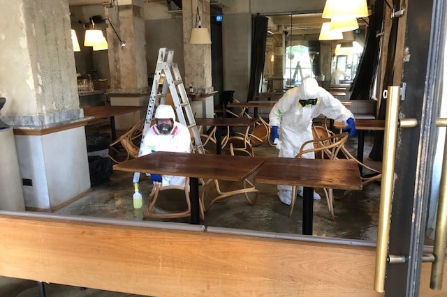 people in hazmat suits wiping down a table in an empty restaurant