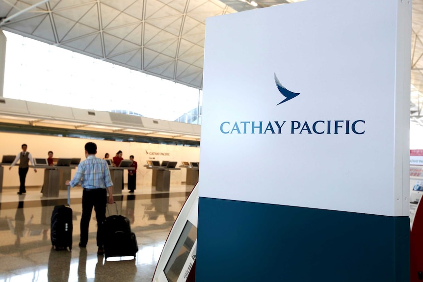 Un pasager care poartă valize se îndreaptă spre un birou Cathay Pacific.