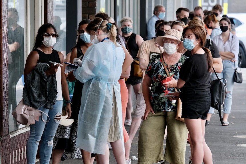 People stand in line wearing masks while someone in PCP takes details.