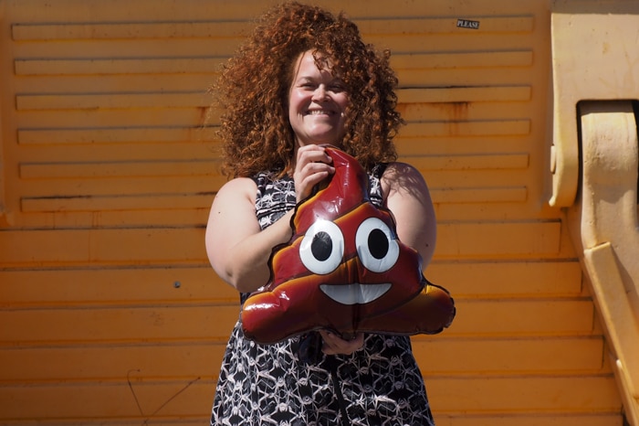 A woman with curly hair smiles as she holds a balloon with a funny face.