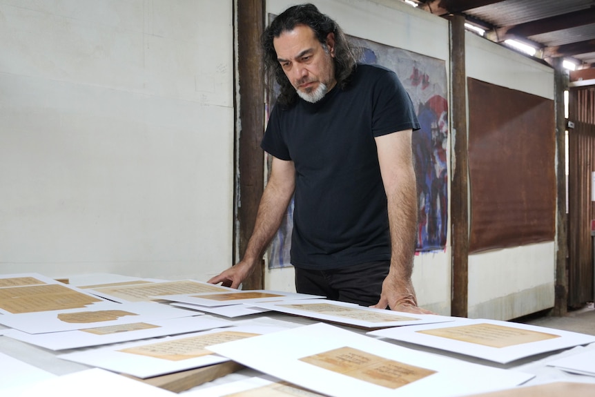 A man looks down at a table covered in print-outs of Quran pages