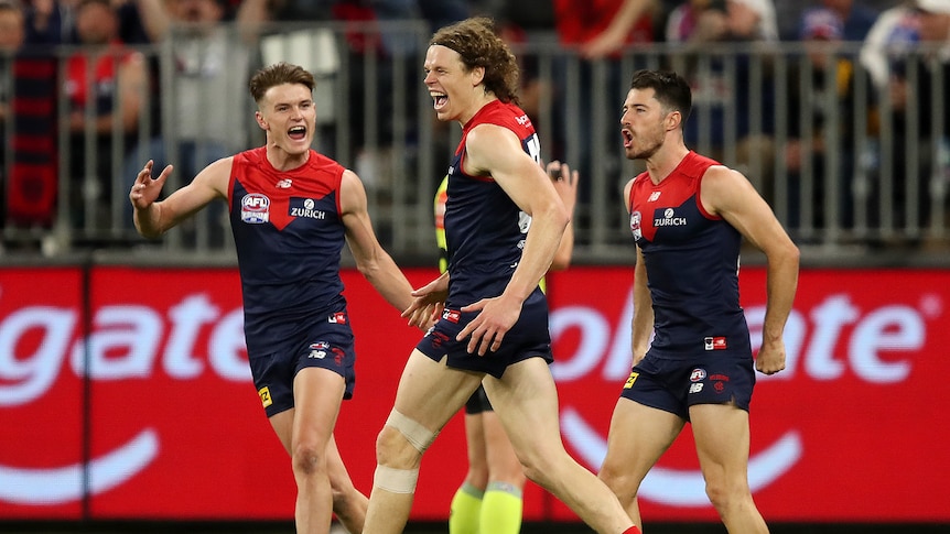 Ben Brown shouts after a goal in between two Melbourne Demons during the AFL grand final.