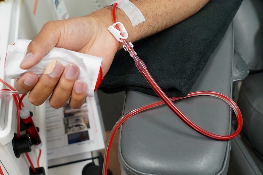 A close-up shows a person's forearm with a tube connected to it below the wrist. There appears to be red liquid in the tube.