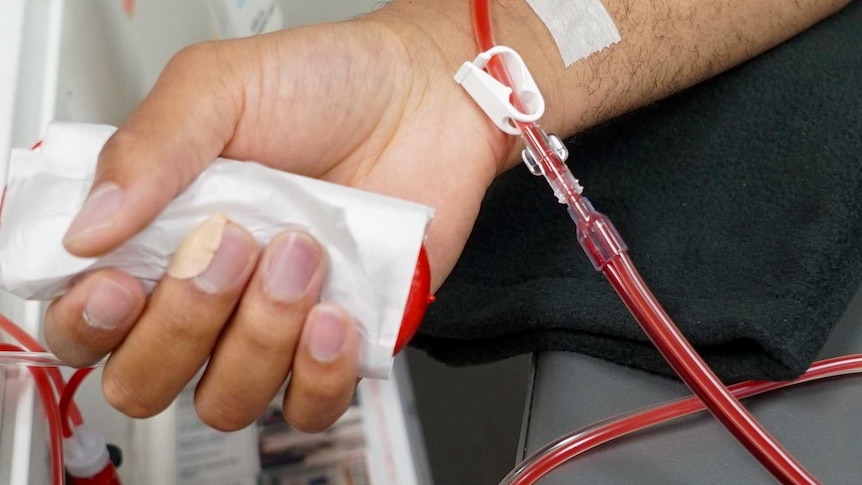 A close-up shows a person's forearm with a tube connected to it below the wrist. There appears to be red liquid in the tube.