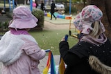 Two young girls wearing pink hats and holding rainbow streamers on an outdoor deck at a childcare centre