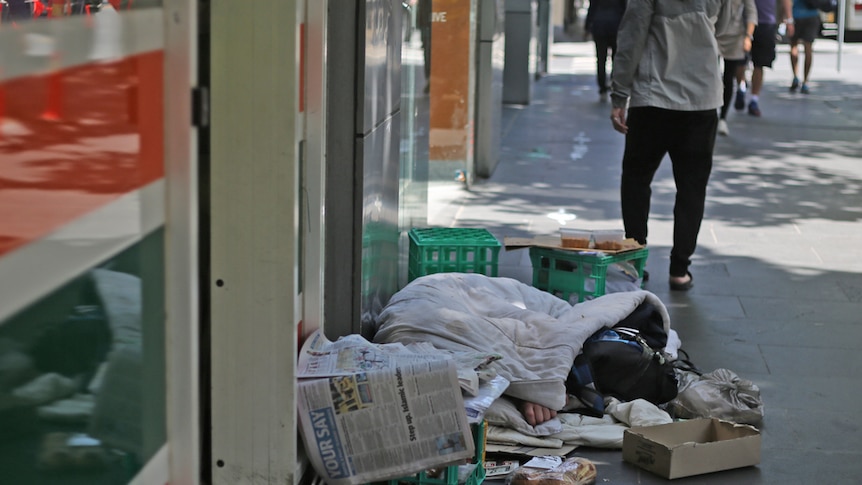 A homeless man sleeps on a street in Melbourne's CBD outside a 7 Eleven.