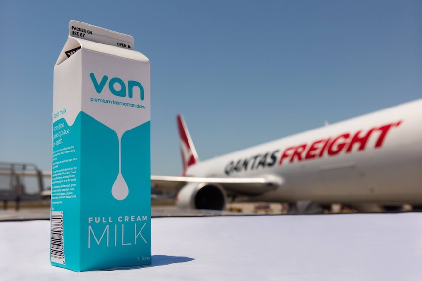 a carton of milk in the foreground with a Qantas Freight plane in the background