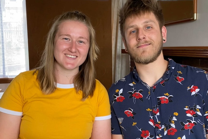 A man and a woman in their early thirties smile in their living room.