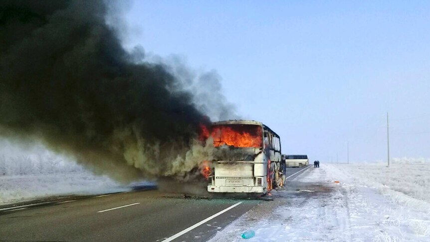 Orange flames an thick black smoke billow from a bus in the middle of a highway surrounded by snow-covered steppes