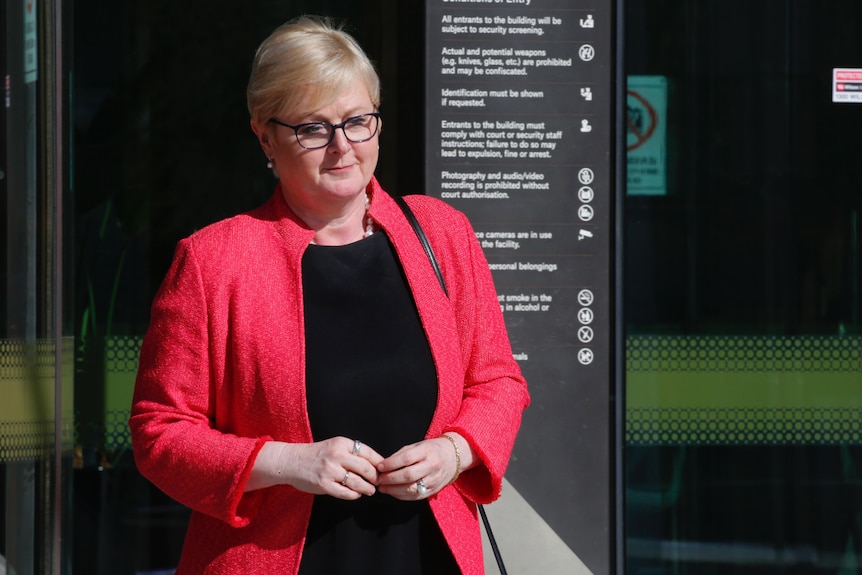 A woman leaving a building in a pink jacket. 