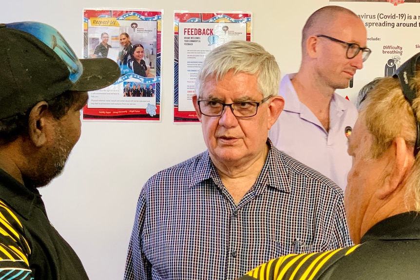 A man with grey hair chats with who other men in a busy room