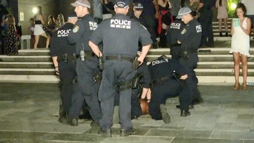 Several police standing over a man on the ground.