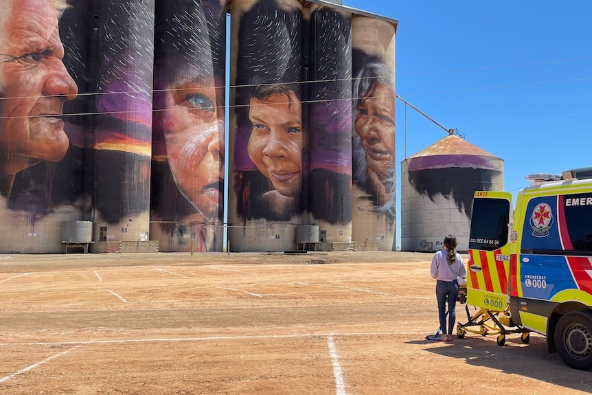 An ambulance sits on the right, with the silo artworks loom in the background 
