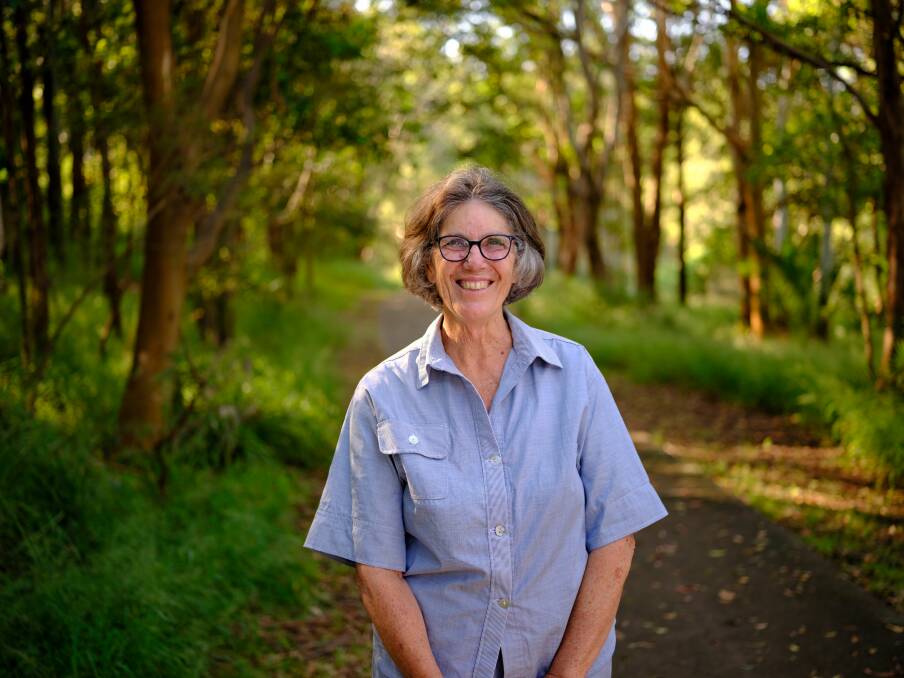 a woman standing near trees smiling at the camera