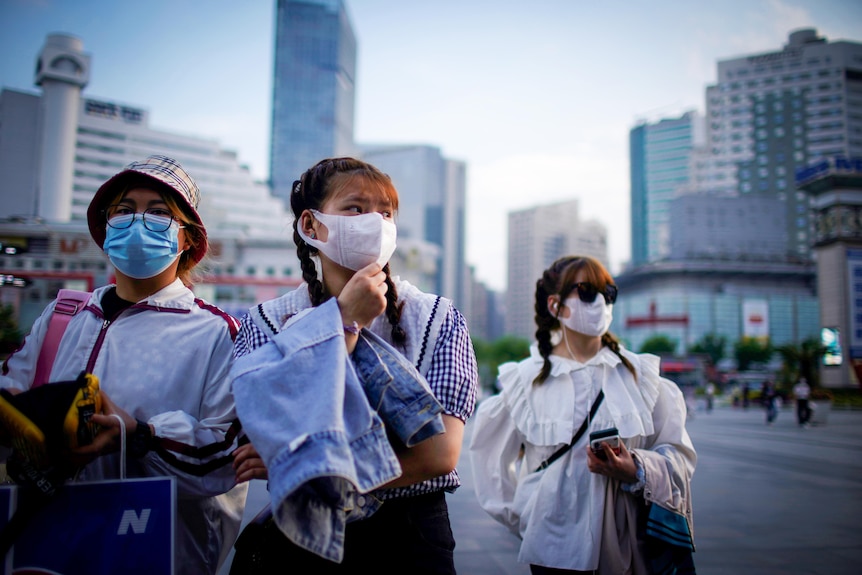 Three young Chinese women in face masks walking through Shanghai CBD