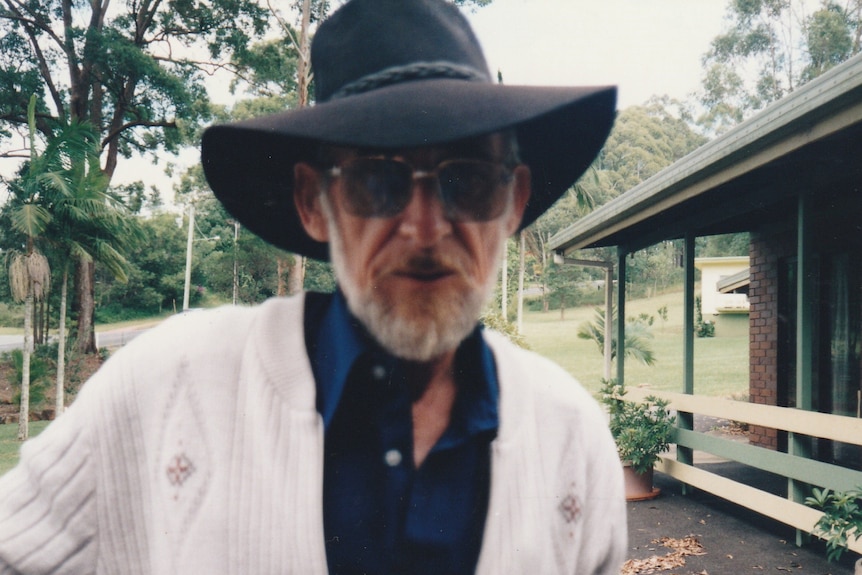 A man wearing a hat and sunglasses looks at the camera