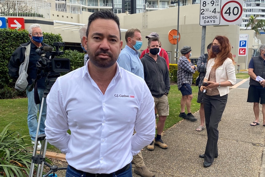 Un hombre con una camisa blanca se encuentra en la frontera de Nueva Gales del Sur con un grupo de comerciantes detrás de él.