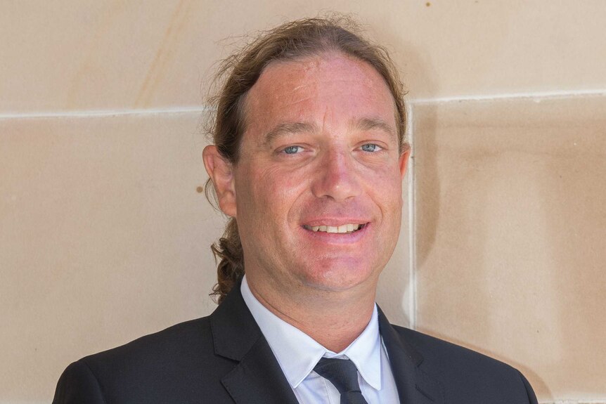 Head shot of a man standing against a sandstone wall