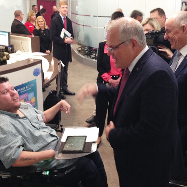 Prime Minister Scott Morrison and NDIS Minister Stuart Robert speak to a disabled man.