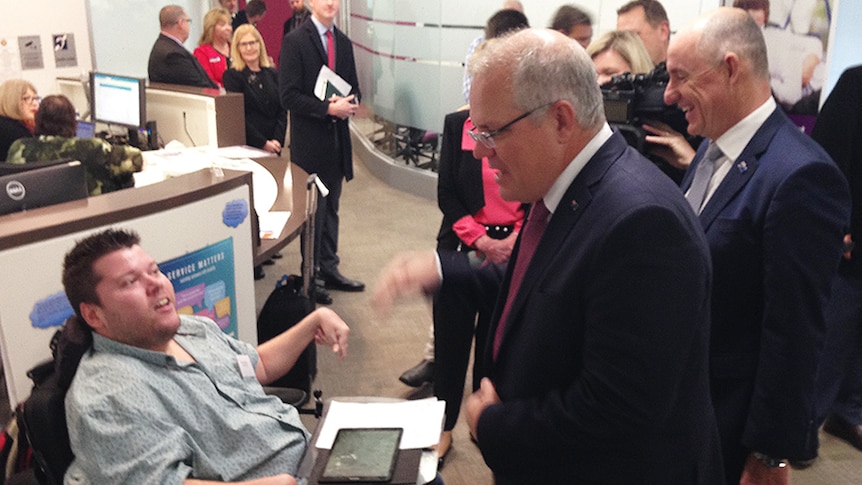 Prime Minister Scott Morrison and NDIS Minister Stuart Robert speak to a disabled man.