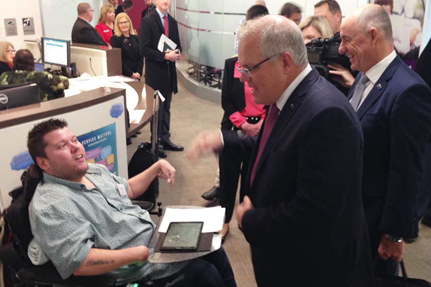 Prime Minister Scott Morrison and NDIS Minister Stuart Robert speak to a disabled man.