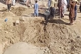 People gather around a crater in the sand 