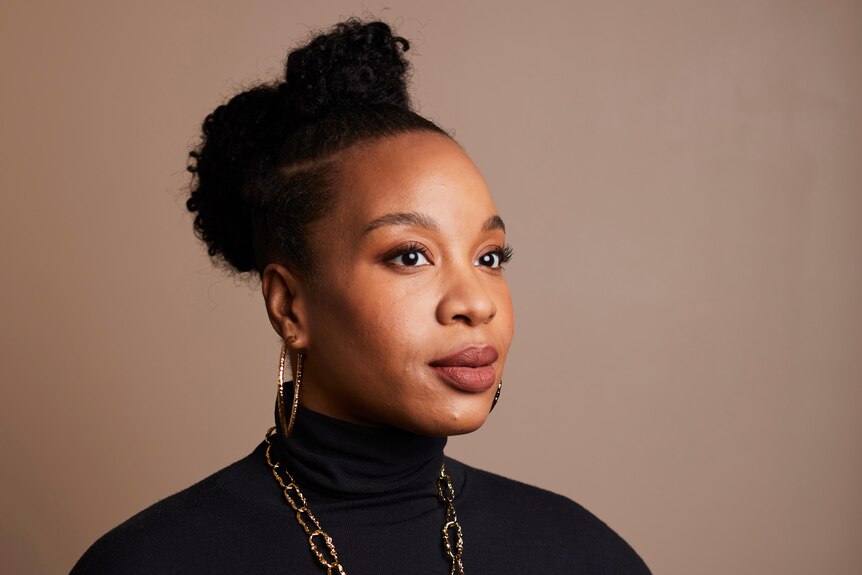 Chinonye Chukwu with her hair in a high bun, in a black turtle neck and gold necklace and hoops, in a formal portrait