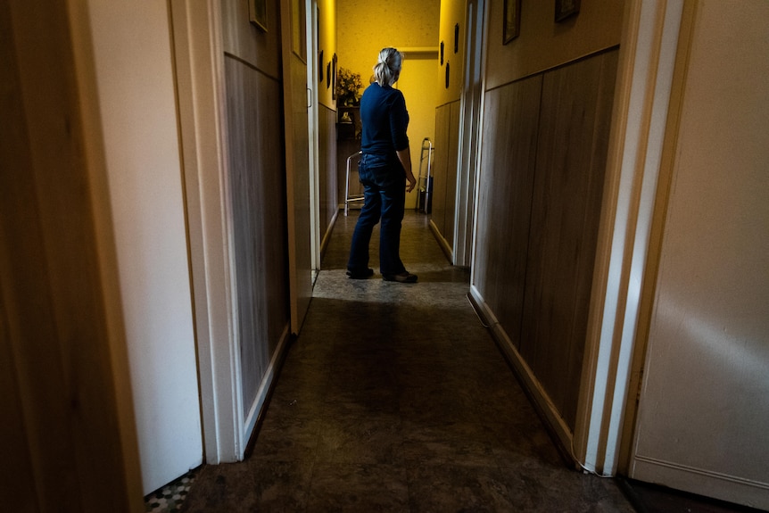 A woman steps into an old, dimly lit hallway.