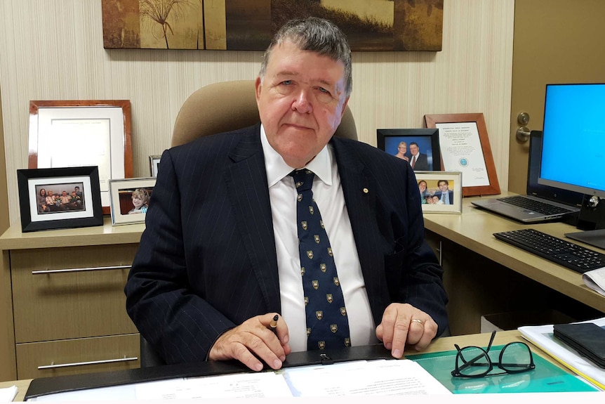 Reverend Keith Garner sits at a desk, pen in hand, looking at the camera.