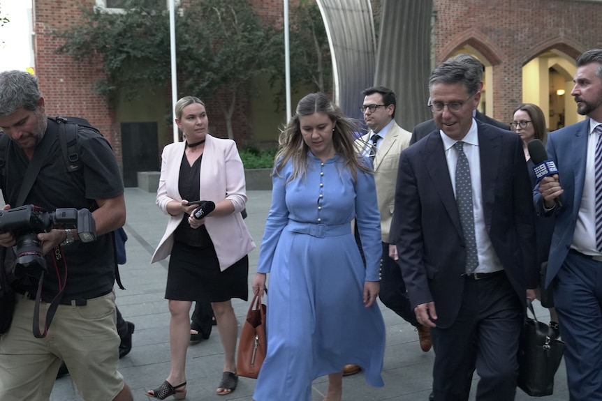 A woman in a blue dress, Brittany Higgins, walks surrounded by other people.