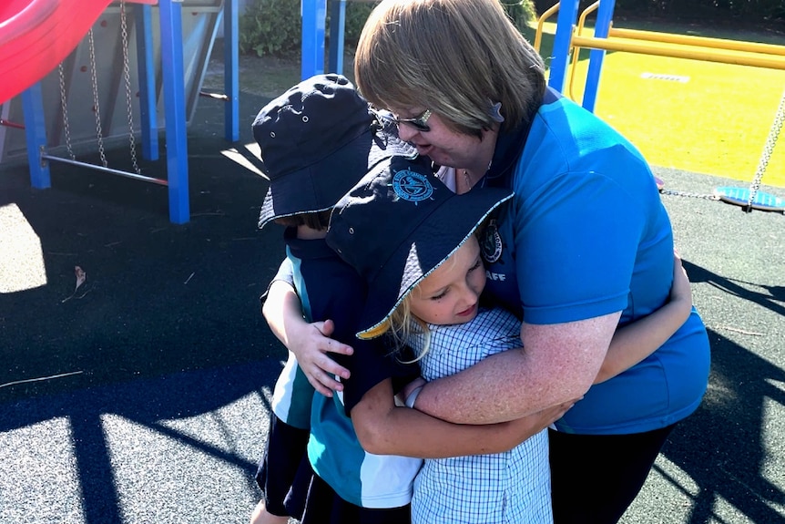 A woman hugging students in a playground.