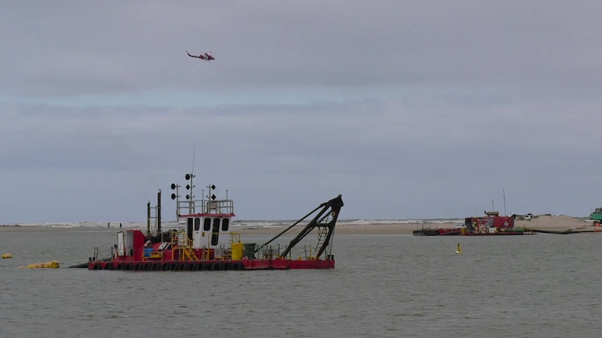 A helicopter flies over boats on a large river