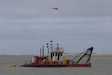 A helicopter flies over boats on a large river