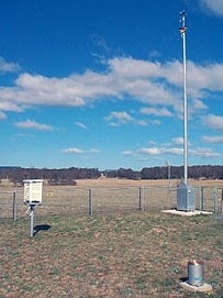     three pieces of technology that form a weather station: a high radar and two boxes on the ground.