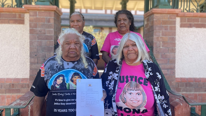 Four women stand outside a courthouse holding a document.