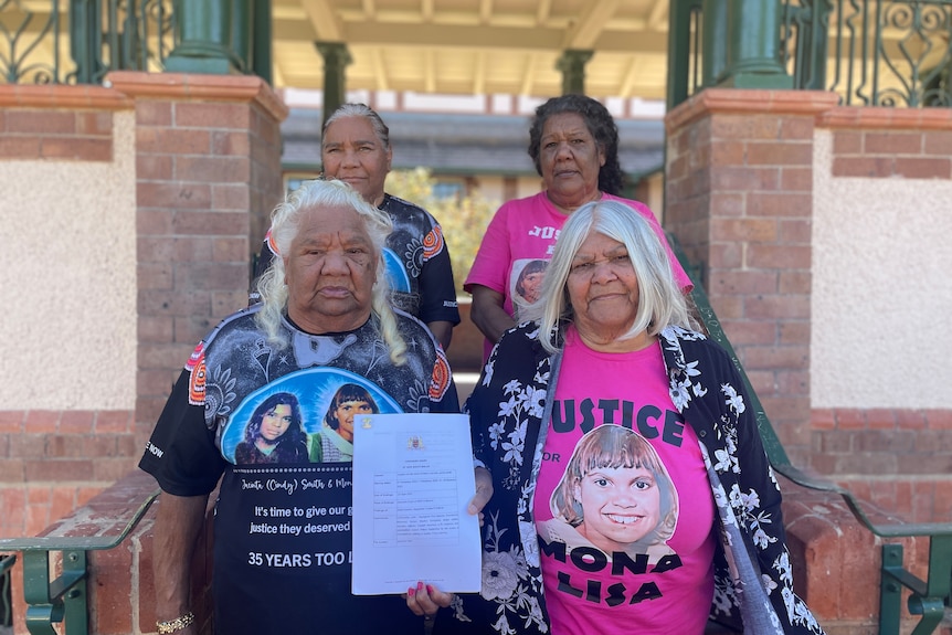 Four women stand outside a courthouse holding a document