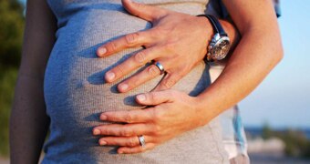 Two hands hold a pregnant belly.
