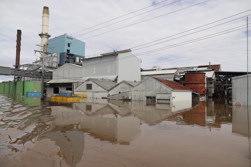 Flood water engulfs industrial sheds, with a smoke stack in the background