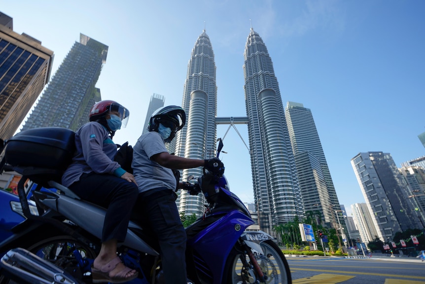 Two people aboard a motorbike wearing face masks in front of Kuala Lumpur's Twin Towers