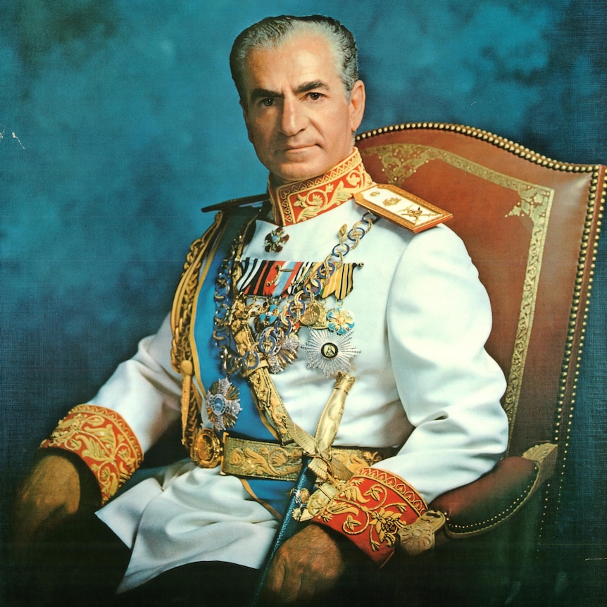 A middle-aged Iranian man wearing a white jacket with many medals and a dagger, sitting on a red chair