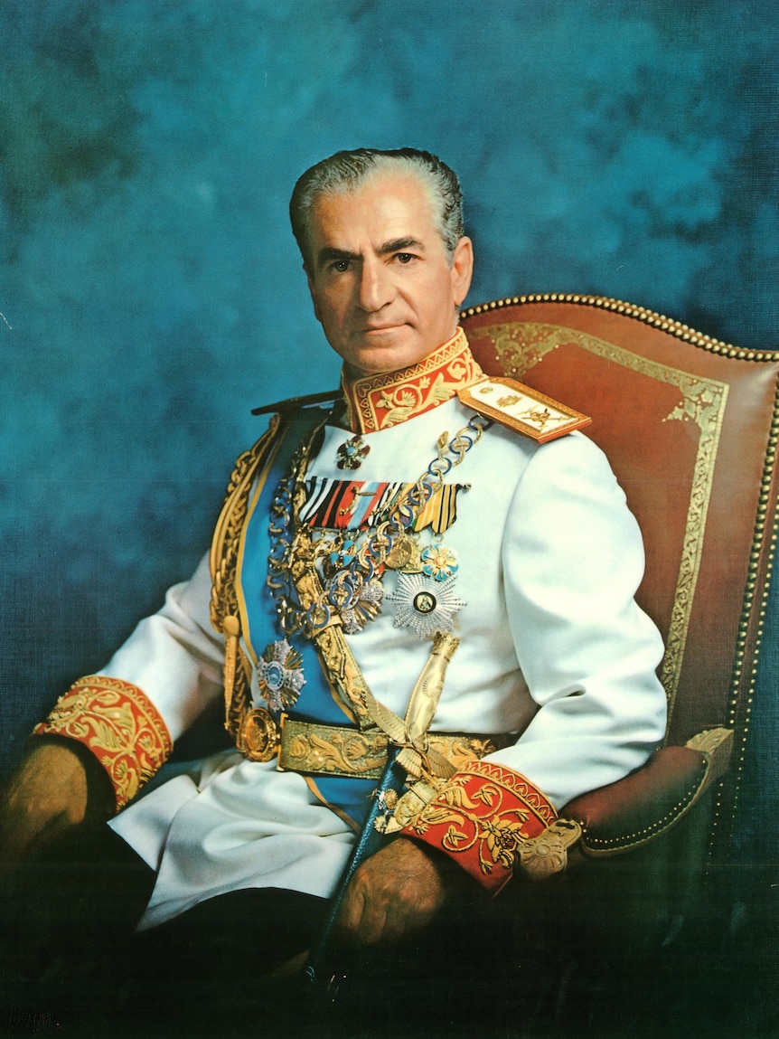 A middle-aged Iranian man wearing a white jacket with many medals and a dagger, sitting on a red chair