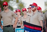 people wearing khaki and red caps holding protest signs