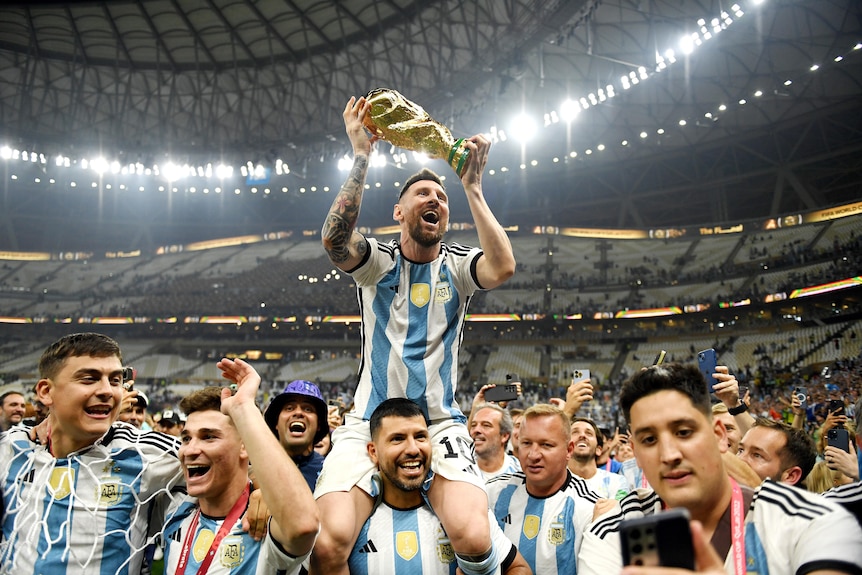 Argentina's Lionel Messi holds the FIFA World Cup trophy while being carried on Sergio Aguero's shoulders after the Qatar final.
