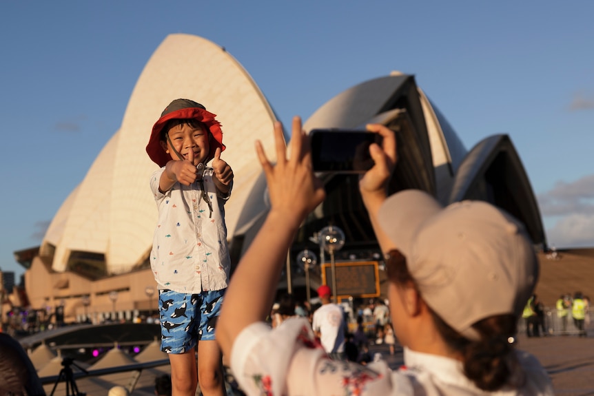 Child stands smiling in front of the Sydney Opera House