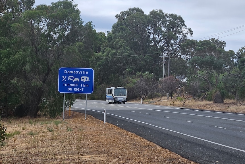 A blue road sign with a photo of a bed and caravan in front of a road where a bus is driving.